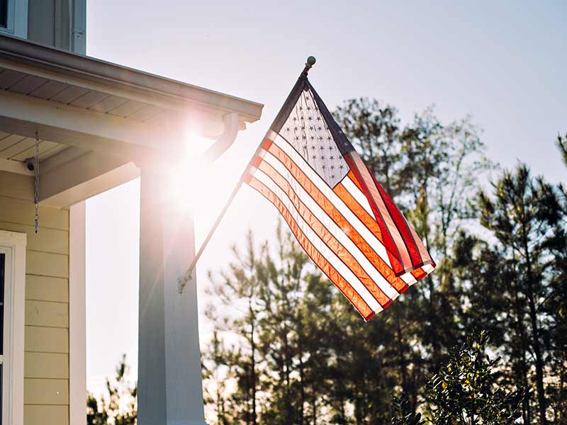 The American flag with the sun behind it, hanging on a home